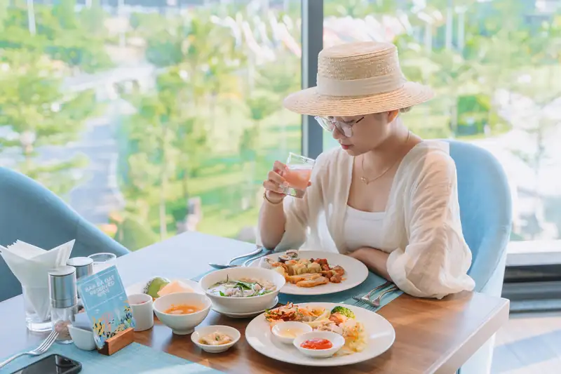 Khách ăn buffet sáng bên cửa kính nhìn ra vườn ở nhà hàng The Blue, Mikazuki Đà Nẵng